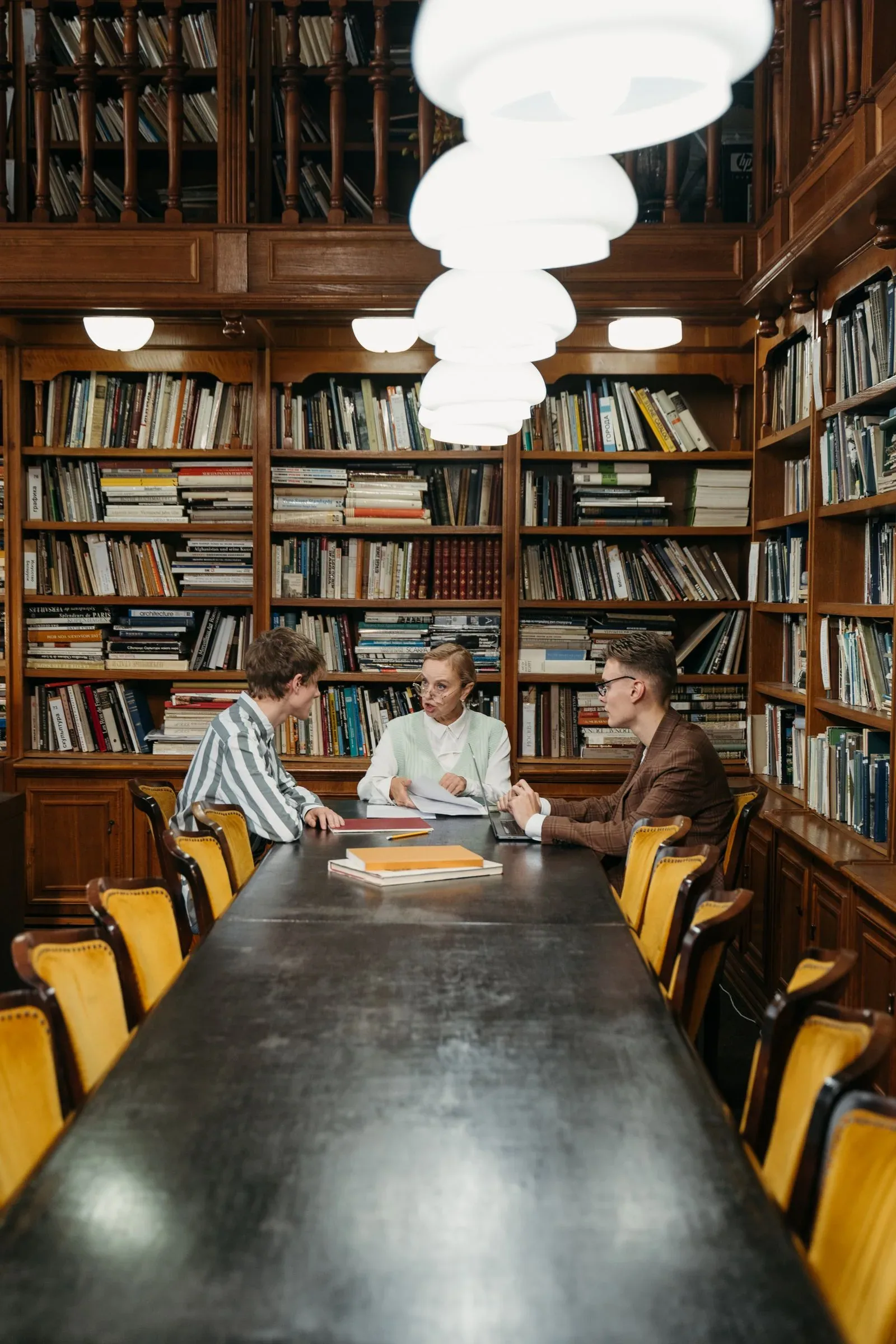 A lecturer and two adult students exchanging ideas in a library